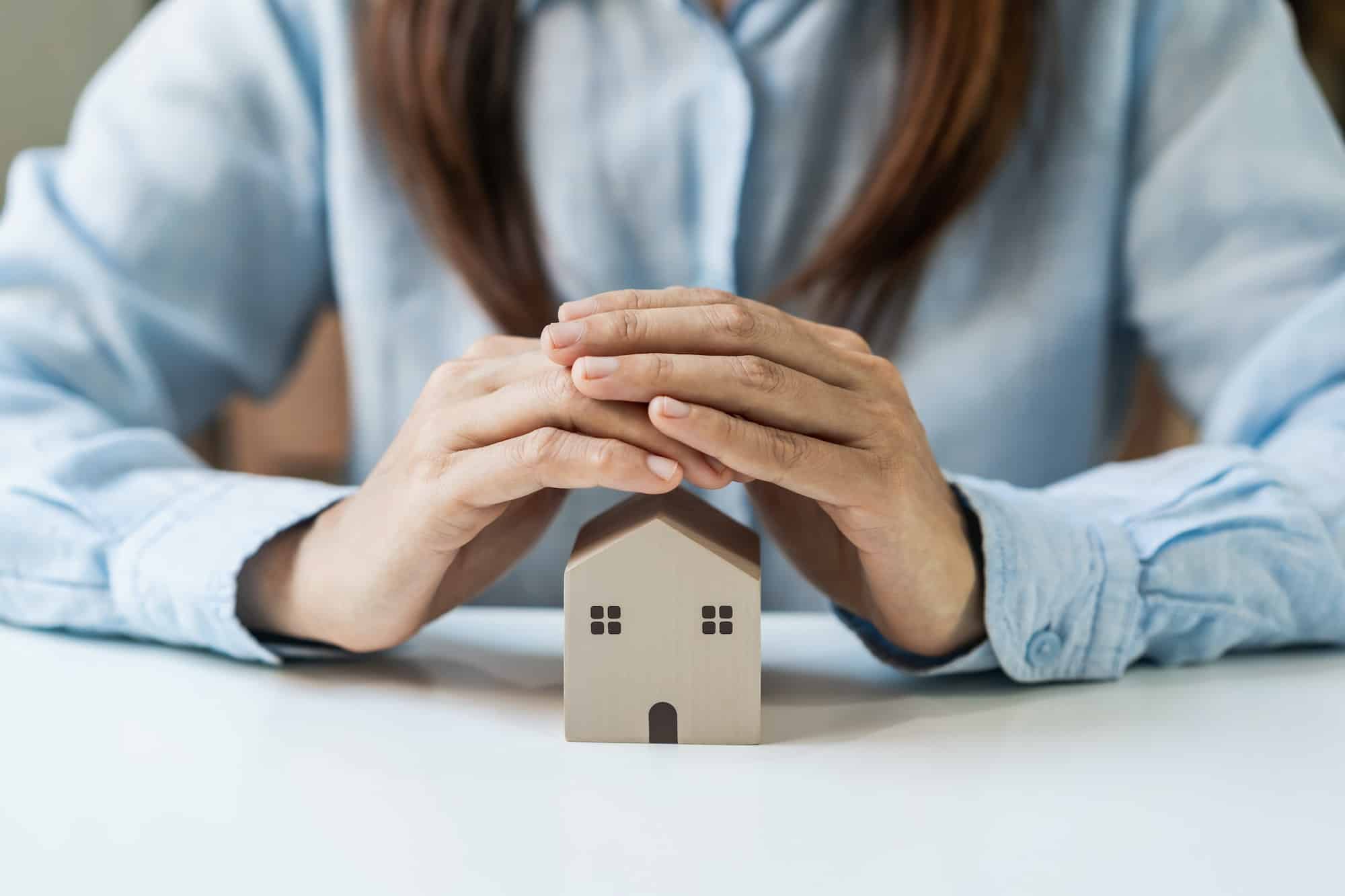 Young woman hands protecting miniature house, Home insurance concept